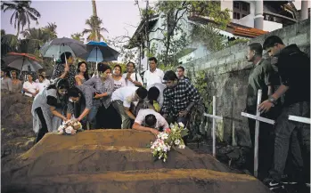  ?? GEMUNU AMARASINGH­E/AP ?? Relatives place flowers after the burial of three victims of the same family who died in a blast at a church in Sri Lanka.