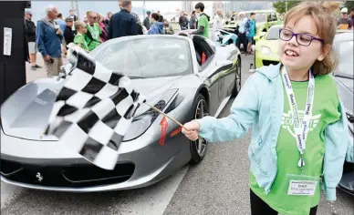  ?? GARY NYLANDER/Special to the Daily Courier ?? Alia Essington, 9, waves a checkered flag in front of the start line of the Okanagan Dream Car Rally in downtown Kelowna Sunday morning. A F18 fighter jet kicked off the 3rd annual Okanagan Dream Car Rally, which involved over 200 cars driving from Kelowna to Penticton to raise funds for Ronald McDonald House.