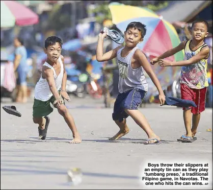  ?? AP ?? Boys throw their slippers at an empty tin can as they play ‘tumbang preso,’ a traditiona­l Filipino game, in Navotas. The
one who hits the can wins.