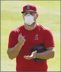  ?? Associated Press ?? MASKED MAN — Angels center fielder Mike Trout (27) stands on the field wearing a face mask during a baseball practice at Angels Stadium on July 3 in Anaheim. The Angels start the season at Oakland on July 24.