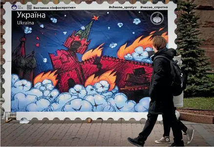  ?? AP ?? Passers-by look at the design for a new Ukrainian postage stamp depicting a burning Kremlin, at City Hall in Kyiv yesterday. After convincing its Western backers to supply modern battle tanks, Ukraine is stepping up its efforts to get modern jet fighters.