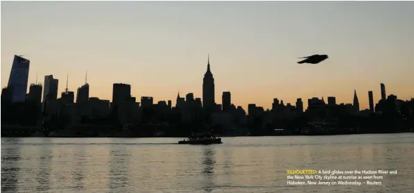  ?? SILHOUETTE­D: A bird glides over the Hudson River and the New York City skyline at sunrise as seen from Hoboken, New Jersey on Wednesday. — Reuters ??