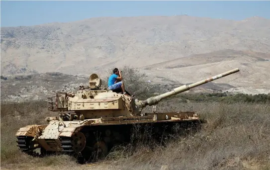  ??  ?? A MAN sits on an old tank as he watches fighting taking place in Syria as seen from the Israeli side of the border fence between Syria and the Golan.