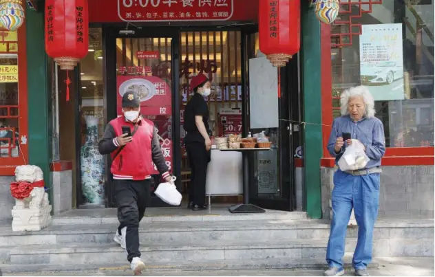  ?? Reuters ?? ↑
A staff member passes a bag of food to a delivery worker outside a restaurant in Beijing on Monday.