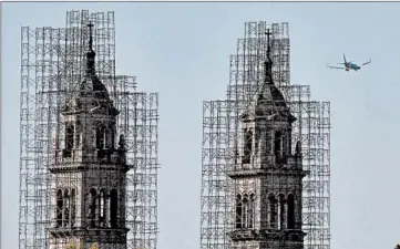  ?? ANTONIO PEREZ/CHICAGO TRIBUNE ?? Scaffoldin­g remains on the twin towers of St. Adalbert Catholic Church in Pilsen as a jet plane flies past Oct. 13.