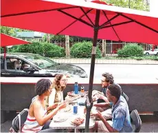  ??  ?? (Clockwise from foreground left) diners Simone Collins, Bernadette Myers, Gianmarco Saretto and Peter Njenga eat pizza at a table set up in the street in front of Mama’s Too in Manhattan.