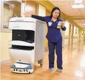  ?? LLOYD FOX/BALTIMORE SUN ?? Gladys Delfin, a registered nurse at Sinai Hospital, takes medication from Tug, a delivery robot, after it stopped at the nurses’ station.