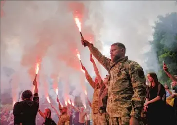  ?? Natacha Pisarenko Associated Press ?? SOLDIERS HOLD f lares during the Kyiv funeral Saturday of Roman Ratushnyi. The soldier and activist, 24, was killed on the eastern front June 9. Ratushnyi had “a heart full of love for Ukraine,” one mourner said.