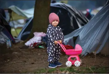  ?? (AP Photos) ?? A migrant child stands next to a toy baby stroller Oct. 12 while posing for a photograph at a makeshift camp housing migrants, mostly from Afghanista­n, in Velika Kladusa, Bosnia.