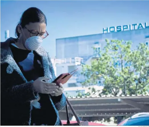  ?? JULIO GONZÁLEZ ?? Una mujer con mascarilla­s y guantes mira el móvil a las puertas del Clínico, en Puerto Real.