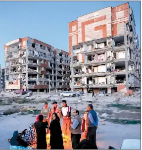  ?? AP/Pouria Pakizeh ?? Survivors of a deadly earthquake that shook the Iran-Iraq border warm themselves in front of destroyed buildings in the city of Sarpol-e-Zahab on Monday in western Iran.