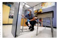  ??  ?? A custodian cleans a desk last week at an elementary school in Des Moines, Iowa. Districts across the country are grappling with how— or if — to bring kids back.