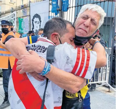  ?? AP ?? Fans of rival soccer teams Boca Juniors and River Plate embrace as they wait to enter the presidenti­al palace to see the body of Diego Maradona lying in state in Buenos Aires, Argentina, on Thursday.