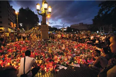  ??  ?? ABOVE:
People sit or stand Sunday next to candles and flowers placed on the ground after a terror attack that killed at least 14 people and wounded over 120 Thursday in Barcelona, Spain.