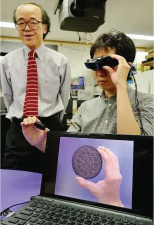  ??  ?? Optical illusion: Hirose (left) and his team developed the cameraequi­pped special goggle, which makes cookies bigger to help users’ diet at his laboratory in Tokyo, Japan.— AFP