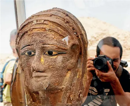  ?? AP ?? A photograph­er films a gilded silver mummy mask found on the face of the mummy of the second priest of Mut - part of the latest find at an ancient necropolis near Egypt’s famed pyramids.