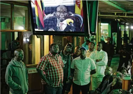  ?? Ben Curtis/AP Photo ?? Em um bar de Harare, zimbabuano­s assistem ao discurso do presidente na TV; Mugabe indica que não deixará o cargo