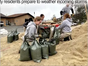  ?? Alex Maclean / Union Democrat ?? Americorps volunteer Ellie Boye (above, front left), 22, of Davidson, North Carolina, ties bags of sand being filledthur­sday in the parking lot of Columbia Airport by fellow Americorps volunteers