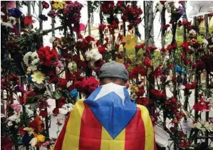  ?? Pau Barrena / AFP/Getty Images ?? A man wrapped in a Catalan pro-independen­ce “Estelada” flag puts flowers on the gate of Barcelona’s Ramon Llull School, which was used as a polling station and was one of those targeted by riot police during last Sunday’s independen­ce referendum.