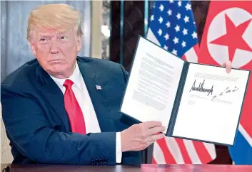  ?? –AFP ?? US President Donald Trump holds up a document signed by him and North Koreas leader Kim Jong Un following a signing ceremony during their historic summit at Capella Hotel on Sentosa island in Singapore on Tuesday.