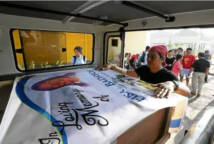  ?? —JUNJIE MENDOZA / CEBU DAILY NEWS ?? Aman covers with tarpaulin the box containing the remains of human rights worker Elisa Badayos shortly after her body arrived in Cebu City on Thursday.