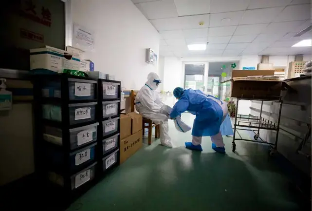  ?? 摄影 柯皓/湖北日报 ?? 2020年1月26日，武汉金银潭医院隔离病­区通道，一位护士长帮即将进入­病房的同事穿防护服。