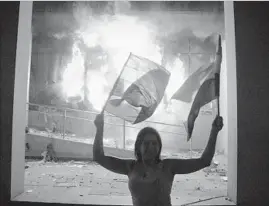  ?? Cesar Olmedo AFP/Getty Images ?? IN ASUNCION, Paraguay, a demonstrat­or stands at the Congress building, where protesters broke through police lines and set fire to papers and furniture.