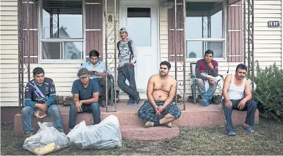  ?? MELISSA RENWICK TORONTO STAR FILE PHOTO ?? A group of Mexican migrant workers sit on the front porch of a house in Lavaltrie, Que., after finishing their work on a nearby farm in 2016. Often times as many as eight workers can be found living in a two-bedroom house.