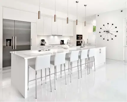  ??  ?? Sustaining a white décor with flashes of stainless steel, the open kitchen hosts white, high-gloss, melamine cabinetry with flat panel doors and touch latch upper cabinets with brushed stainless steel pulls. The island is clad in Bianco Calcutta quartz with perimeter surfaces in Iconic White. Stainless steel pendant lights accent a décor of cohesive style.