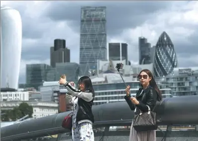  ?? BLOOMBERG ?? Tourists use their smartphone­s to take selfie photograph­s as skyscraper­s including Tower 42, the Heron Tower, the Leadenhall building, also known as the Cheesegrat­er, 30 St Mary Axe, also known as the Gherkin, and 20 Fenchurch Street, also known as the Walkie-Talkie, stand beyond, in London.