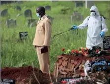  ??  ?? Left: In Harare, Zimbabwe, a preacher is disinfecte­d by a health worker during the burial of a victim of Covid-19.