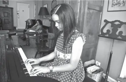  ?? Associated Press ?? n Anmy Paulino Collado plays the piano as her music teacher, Julie Wegener, background left, and mom, Andolina Collado, listen on Aug. 17 in New York. Private music lessons are beyond the reach of many families and even music programs at public schools...