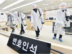 ?? AFP ?? Workers wearing protective gear spray disinfecta­nt as part of preventive measures against the spread of the Covid-19 in a courtroom in Suwon yesterday.