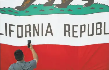  ?? Paul Kuroda / Special to The Chronicle 2019 ?? A man photograph­s the California state flag at Laney College in Oakland in 2019. The California dream isn’t attainable for a skyrocketi­ng number of residents who can’t afford to buy or rent a decent home.