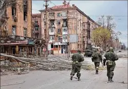  ?? Alexei Alexandrov / Associated Press ?? Servicemen of Donetsk People's Republic militia Saturday walk past damaged apartment buildings near the Illich Iron & Steel Works Metallurgi­cal Plant, the second largest metallurgi­cal enterprise in Ukraine, in an area controlled by Russian-backed separatist forces in Mariupol, Ukraine.