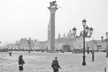  ?? — Reuters photo ?? People walk in flooded Saint Mark Square during a period of seasonal high weather in Venice, Italy.