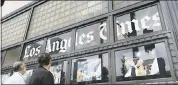  ?? THE ASSOCIATED PRESS ?? Passersby look at news photos posted outside the Los Angeles Times building in downtown Los Angeles.