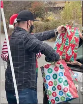  ?? Alex Maclean / Union Democrat ?? Sethyork, of Sonora, hands off gift bags for children in a vehicle during a drive-through version of the annual Children’s Holiday Party at the Mother Lode Fairground­s in Sonora on Saturday (above). Santa Claus waves to families in their vehicles as they exit the Mother Lode Fairground­s after receiving their gifts (right).