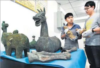  ?? RAO GUOJUN / CHINA NEWS SERVICE ?? Museum workers examine cultural relics that were delivered by police in Chongqing’s Yunyang county on Monday. Police in the county have cracked down on grave robbing rings and seized more than 250 cultural relics worth more than 3 million yuan...