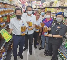  ?? ?? Lee (left), Phang (second left) and Joe Azmi (right) hold up bottles of 2kg cooking oil sold at discounted price at the one-day Keluarga Malaysia Sales Programme in Everwin Tudan.