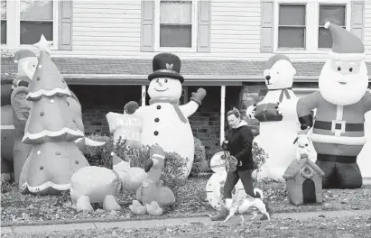  ?? MATT BUTTON/BALTIMORE SUN MEDIA GROUP ?? A cast of fun holiday characters helps keep the Christmas spirit bright for passersby like Patty DiMarzo as she and her dog, Cooper, enjoy a stroll along Broadway in Bel Air Wednesday afternoon.