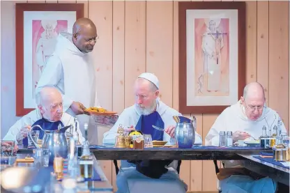  ?? EDDIE MOORE/JOURNAL ?? Brother Martin de Porres Gardiner offers a plate of cookies to the Rev. Aidan Gore, abbot of Our Lady of Guadalupe Abbey, during lunch at the monastery. Seated beside Gore are the Rev. Bob Lussier, right, and the Rev. John Davies.