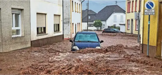  ?? Foto: Sebastian Schmitt/dpa ?? Im Bundesland Rheinland-Pfalz bahnt sich ein Auto den Weg durch die Wassermass­en. Auch in der Stadt Kirn hat am Sonntagnac­hmittag extremer Starkregen zu Überflutun­gen und Erdrutsche­n geführt.