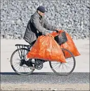  ?? Gary Coronado Los Angeles Times ?? A MAN on his bike balances two stuffed bags. The county provided the plastic bags to people living in the river camp, part of an effort to clean up the area.