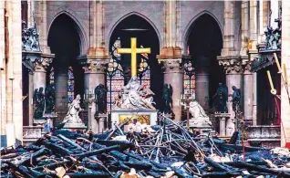  ?? (Reuters) ?? SPARED – The cross and sculpture of Pieta by Niclas Coustou stand amid the debris inside the Notre Dame cathedral, Wednesday, a day after the fire that destroyed the church’s roof and spire. The sculpture was among the precious artworks that survived the nine-hour blaze.