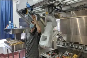 ?? Miso Robotics via AP ?? A technician makes an adjustment to a robot July 9 at Miso Robotics’ White Castle test kitchen in Pasadena, Calif. Robots that can flip burgers, make salads and even bake bread are in growing demand as virus-wary kitchens try to put some distance between workers and customers. Starting this fall, the White Castle burger chain will test the robot arm that can cook french fries and other foods. The robot, dubbed Flippy, is made by Pasadena, California-based Miso Robotics.