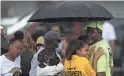  ?? BESSEX/AP JOSHUA ?? Bystanders gather under an umbrella as rain rolls in after a shooting at a supermarke­t in Buffalo, N.Y.