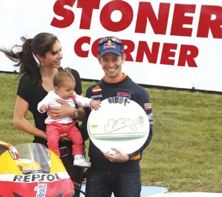  ?? Repsol Honda team rider Casey Stoner of Australia right, wife Adriana and baby Alessandra stand in front of the newly named Stoner Corner during the MotoGP Australian Motorcycle Grand Prix in Phillip Island, Australia, yesterday. Andrew Fox of Linfox Prop ??