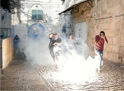  ?? PHOTO: REUTERS ?? Palestinia­ns react as a stun grenade explodes in a street at Jerusalem’s Old City outside the compound known to Muslims as Noble Sanctuary and to Jews as Temple Mount, after Israel removed all security measures it had installed at the compound.