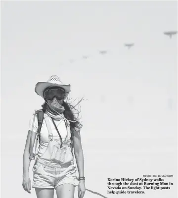  ?? TREVOR HUGHES, USA TODAY ?? Karina Hickey of Sydney walks through the dust at Burning Man in Nevada on Sunday. The light posts help guide travelers.